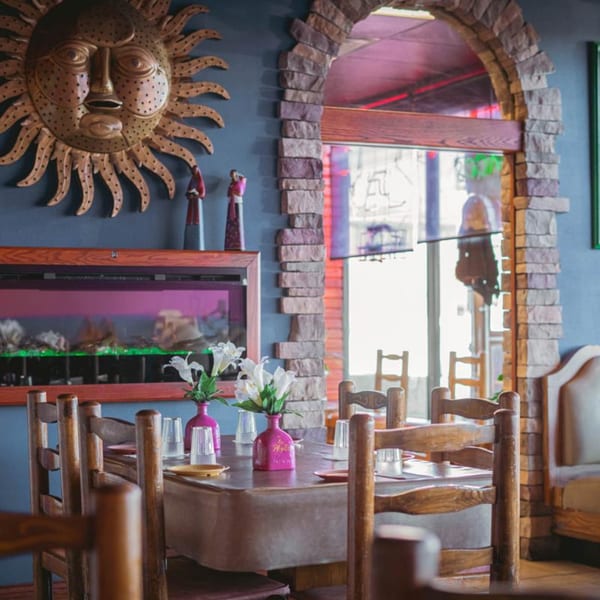 Interior of La Playita Mexican Restaurant with a sun decoration, stone archway, and dining tables.