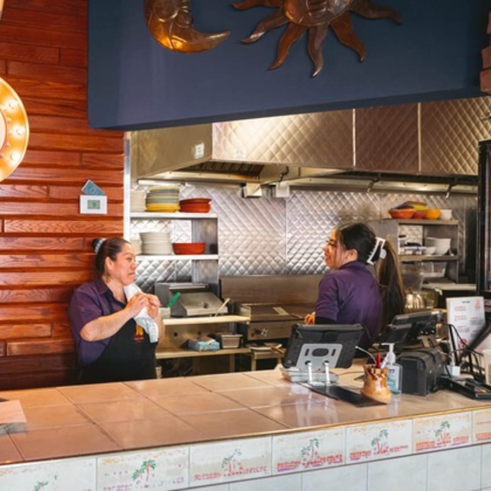 Two women working behind the counter in a Mexican restaurant kitchen with decorative sun and moon.