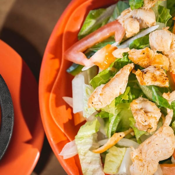 Close-up of a vibrant La Playita Mexican Restaurant chicken salad with lettuce, tomatoes, and onions.