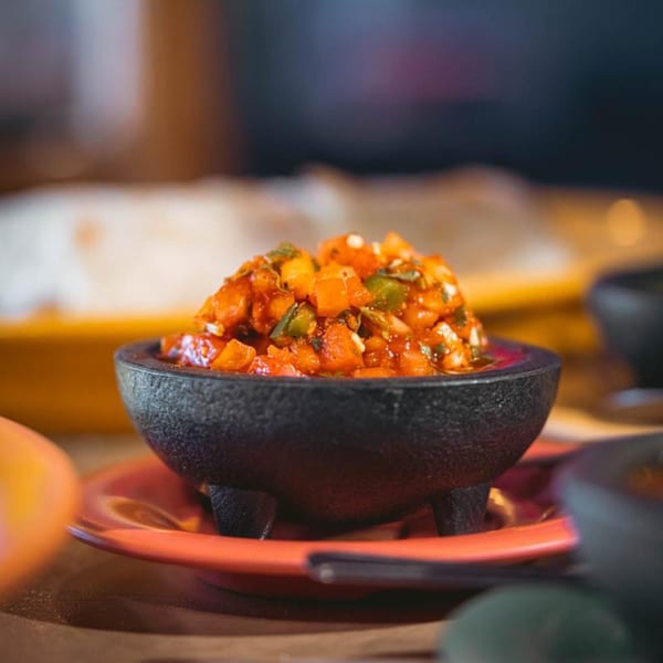 A black molcajete bowl filled with vibrant red salsa, garnished with green peppers and onions.