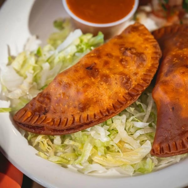 Two golden-brown empanadas on a bed of shredded lettuce with a side of red sauce.