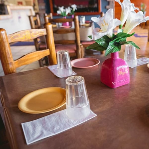 A set table at La Playita Mexican Restaurant with plates, glasses, and a pink Patron vase.