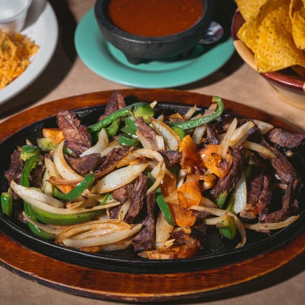 Sizzling beef fajitas with onions and green peppers, served with salsa and tortilla chips.