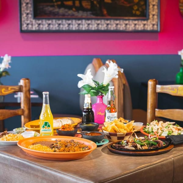 A table laden with various Mexican dishes, including fajitas, rice, beans, chips, and drinks.
