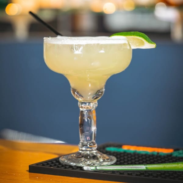 A La Playita Mexican Restaurant margarita with a salted rim, lime wedge, and straw on a bar.